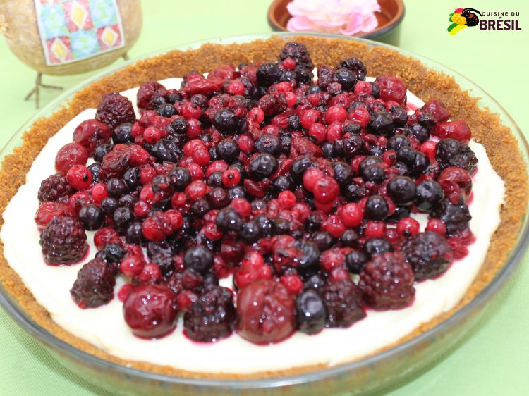 Tarte aux fruits rouges prise sur un fond vert avec une poule en céramique et une fleur rose